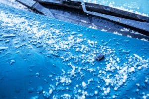 The hood of a car with pieces of hail on it after a storm
